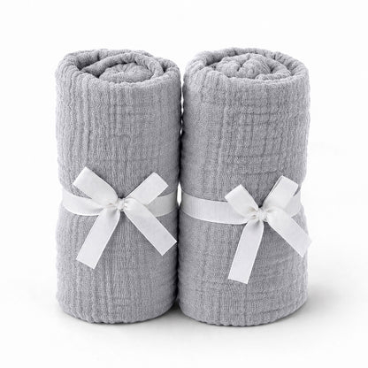 Two rolled-up light gray towels tied with white ribbons rest side by side, evoking the softness and purity of Newton Baby's Breathable, Organic Cotton Sheets (2-pack), set against a plain white background.