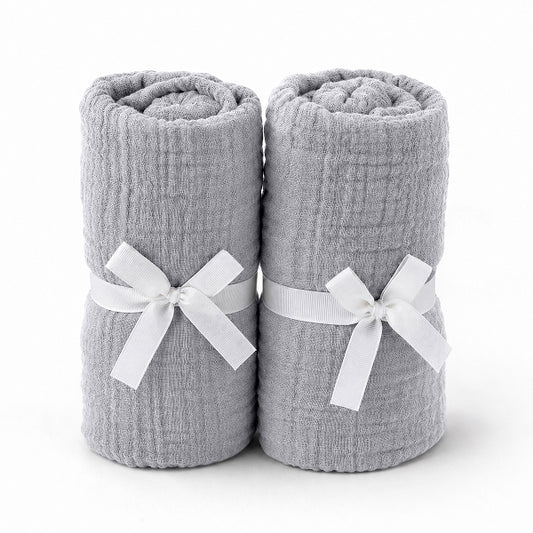 Two rolled-up light gray towels tied with white ribbons rest side by side, evoking the softness and purity of Newton Baby's Breathable, Organic Cotton Sheets (2-pack), set against a plain white background.