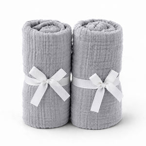 Two rolled-up light gray towels tied with white ribbons rest side by side, evoking the softness and purity of Newton Baby's Breathable, Organic Cotton Sheets (2-pack), set against a plain white background.