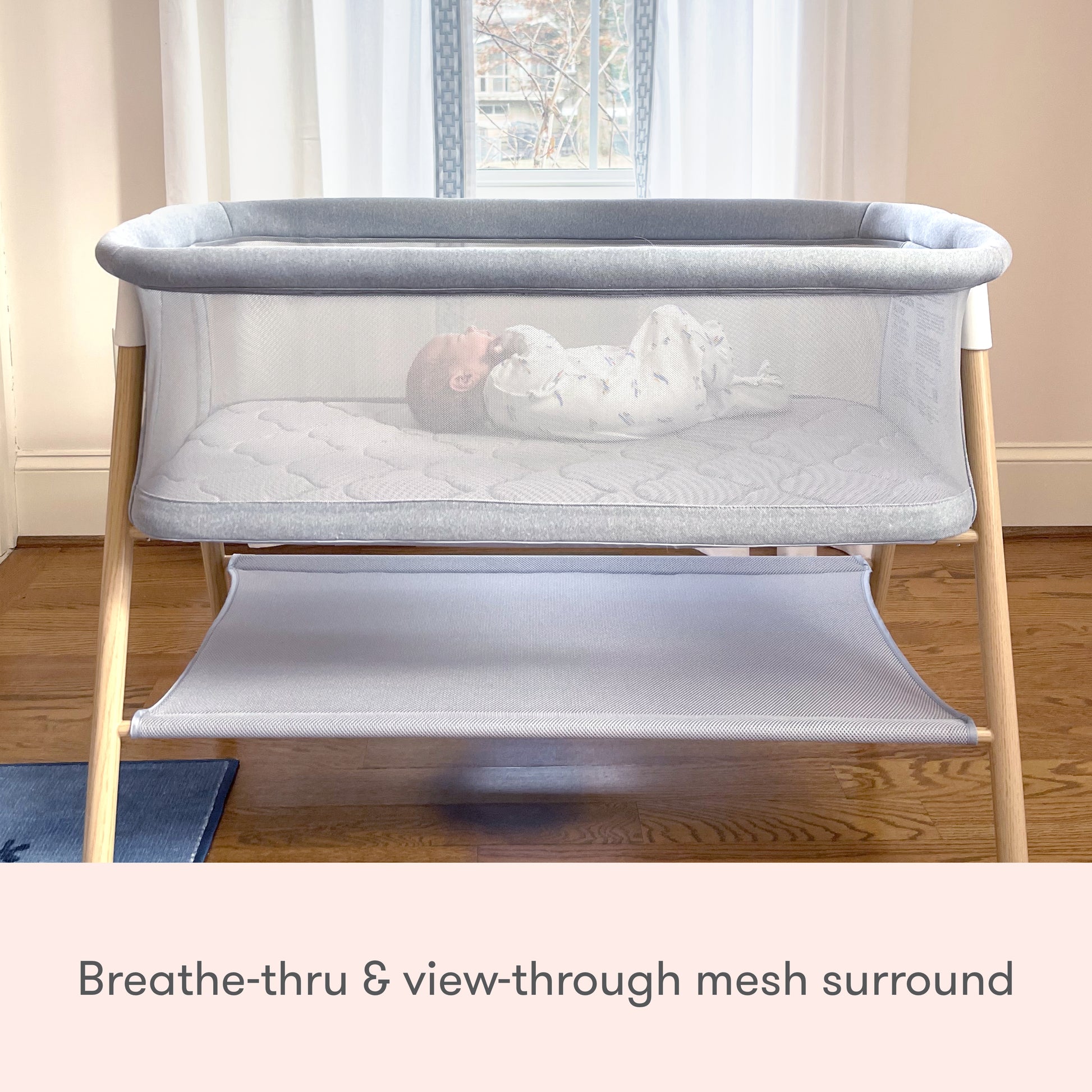 baby lying in essential bassinet, visible through mesh walls, text reads "breathe-thru & view-through mesh surround"