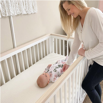 A stylish wooden baby crib with white bedding, plush toys, set in a warmly decorated room.