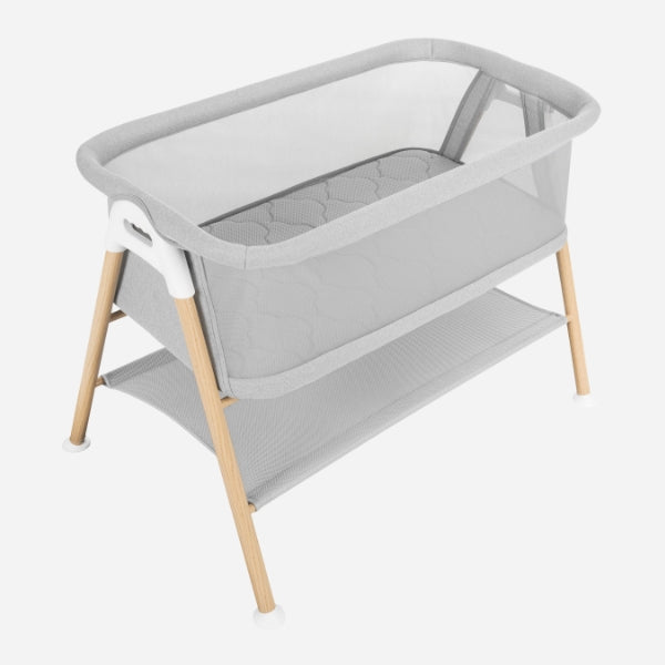 The Newton Baby Essential Bassinet features light wood legs, a soft gray fabric body, mesh sides for breathability, a quilted breathe-thru mattress, and a lower mesh storage shelf.