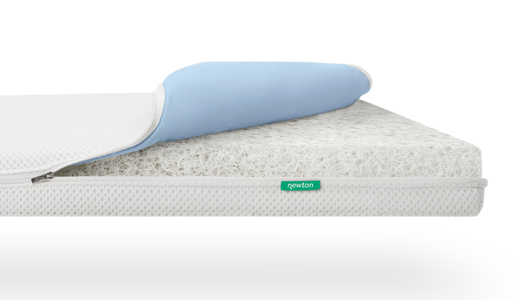 A close-up view of a layered mattress with a white and blue removable cover partially peeled back, revealing a white, mesh-like interior. A green tag labeled newton is attached to the side.