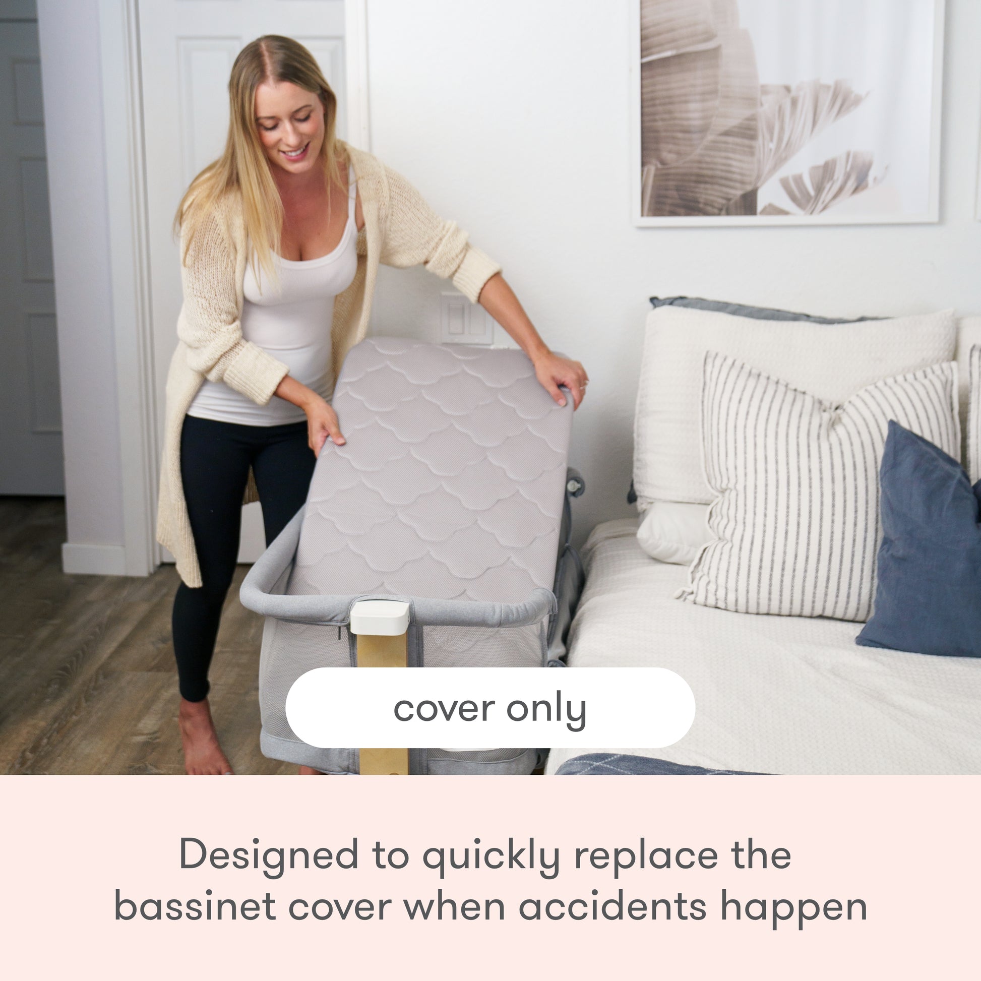 A woman lifts a gray Newton Baby Extra Bassinet Mattress Cover beside a bed. Text reads: “cover only.” Caption: “Easily swap out the machine-washable cover for your bassinet when accidents happen.”.