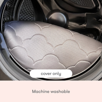 The Newton Baby Extra Bassinet Mattress Cover, featuring a quilted cloud pattern, is placed in a front-loading washing machine. Text on the image reads "cover only" and "machine washable.