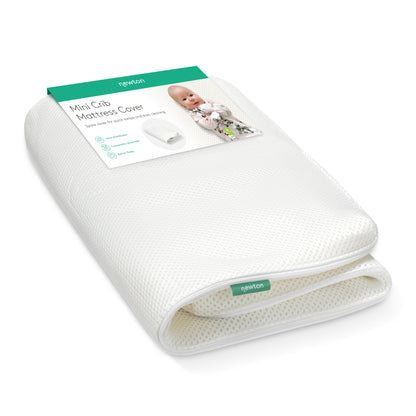 A folded white Extra Mini Crib Mattress Cover by Newton Baby with a green and white label featuring a baby and product details. This washable cover is designed for comfort and convenience.