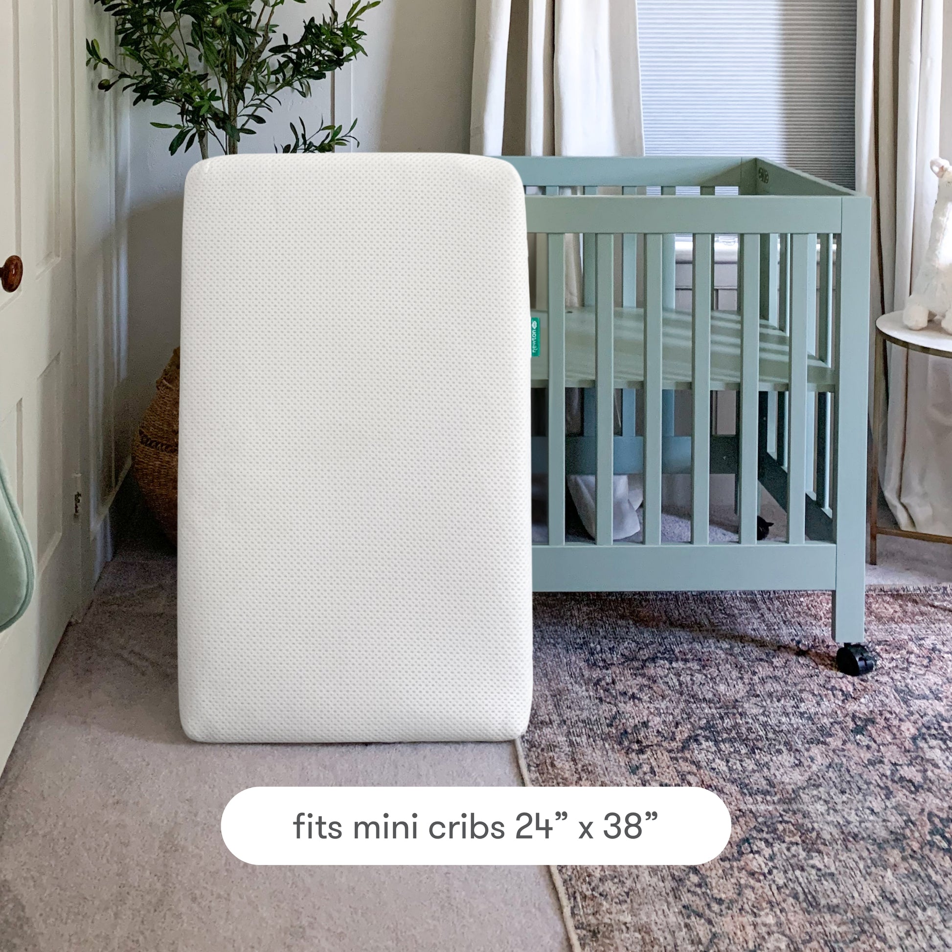 A washable, breathable white Extra Mini Crib Mattress Cover by Newton Baby stands upright in front of a green mini crib. Text reads: Fits mini cribs 24 x 38 with a snug fit for your Newton Baby mattress.