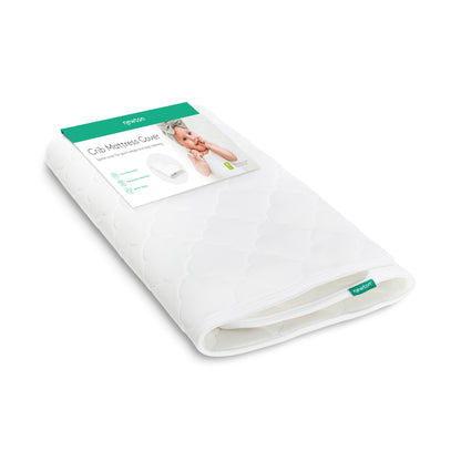 A washable white Extra Original Crib Mattress Cover with a quilted pattern is shown folded. The packaging displays a baby photo and product details, with the Newton Baby brand name clearly visible on the label and tag.