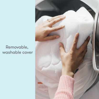 Close-up of hands loading a white, breathable Extra Waterproof Crib Mattress Cover by Newton Baby into a washing machine. Text reads: Removable, washable cover. Perfect fit for your Newton mattress. Light blue background.