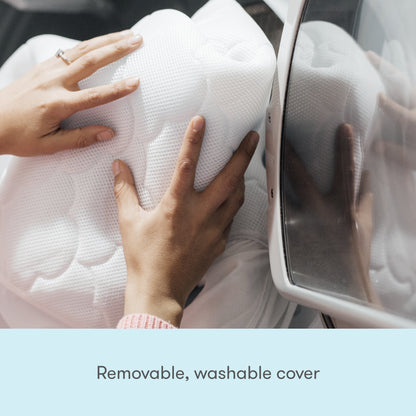 Close-up of hands placing the Newton Baby Extra Waterproof Crib Mattress Cover, featuring a removable, breathable cover, into a washing machine. Text below reads: Removable, washable cover.