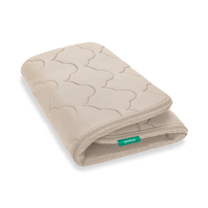 The Newton Baby Extra Bassinet Mattress Cover is beige and rectangular with a quilted wave pattern and a green 