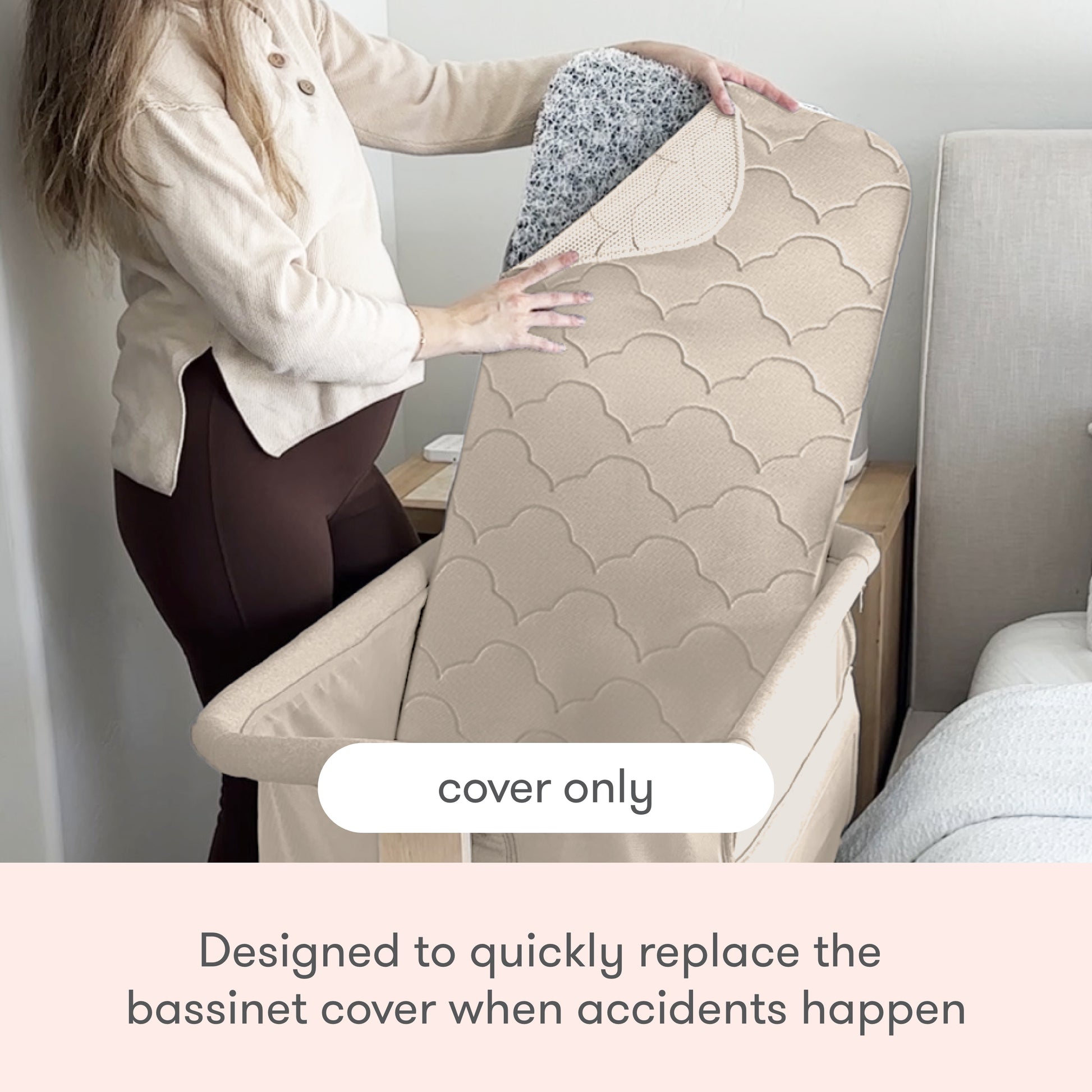 A person lifts a beige, quilted Newton Baby Extra Bassinet Mattress Cover to reveal its speckled underside beside a bed. Text reads: “cover only” and “Easily replace the Bassinet Mattress Cover after accidents. Machine washable.”.