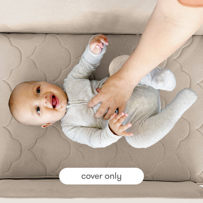 A smiling baby in a gray onesie lies on a quilted mattress as an adult hand gently touches their chest. Text at the bottom reads “Newton Baby Extra Bassinet Mattress Cover only.”.