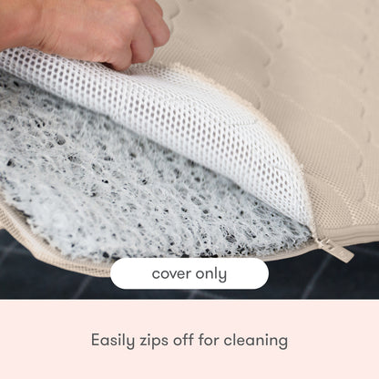 A hand unzips the Newton Baby Extra Bassinet Mattress Cover, revealing a white mesh layer. Text says cover only—easily zips off for cleaning and is machine washable for convenience.
