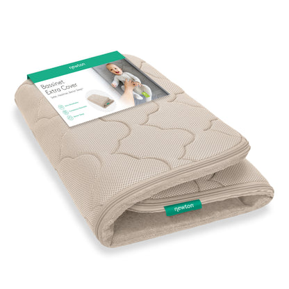 A folded beige Newton Baby Extra Bassinet Mattress Cover with a green and white label showing a smiling baby and details. The “newton” tag is visible. This cover is machine washable. 999-4400-SAN