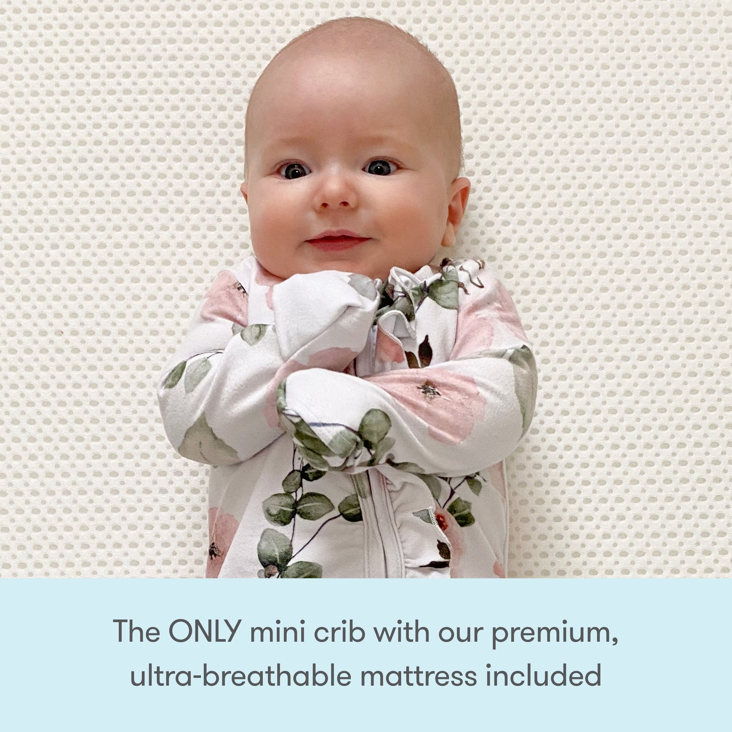 A baby rests in a floral swaddle on the Newton Mattress inside the Newton Galileo Mini Crib by Newton Baby. Text below reads: The ONLY portable crib that includes our premium, ultra-breathable mattress.