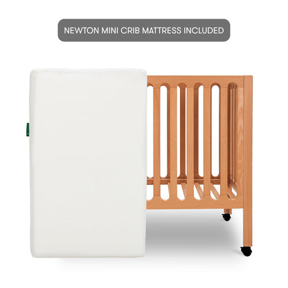 The Newton Galileo Mini Crib with wheels is shown with a white Newton Baby Mini Crib Mattress. A label above reads, "Newton Mini Crib Mattress Included.