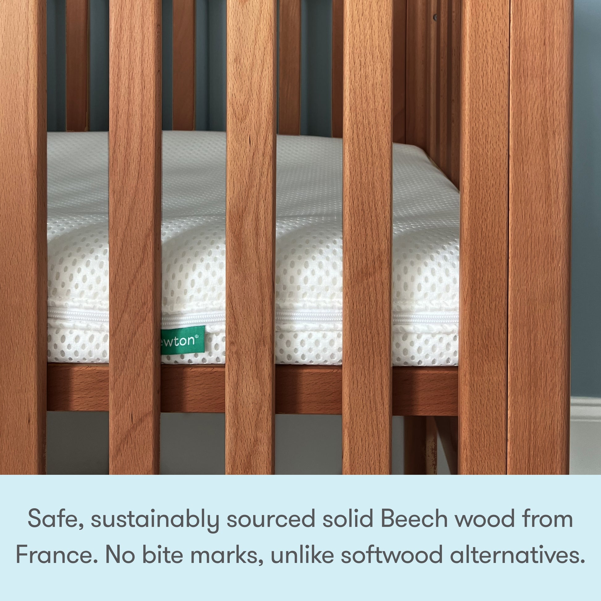 A close-up of the Newton Galileo Mini Crib with Newton Mattress by Newton Baby showcases its solid Beech wood vertical slats and a white mattress with green Newton label, emphasizing superior safety and durability for a sturdy, portable crib.