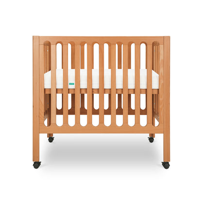 The Newton Baby Galileo Mini Crib with Newton Mattress, crafted from beech wood with vertical slats and four black casters, is shown against a white background—an ideal portable crib for modern nurseries.