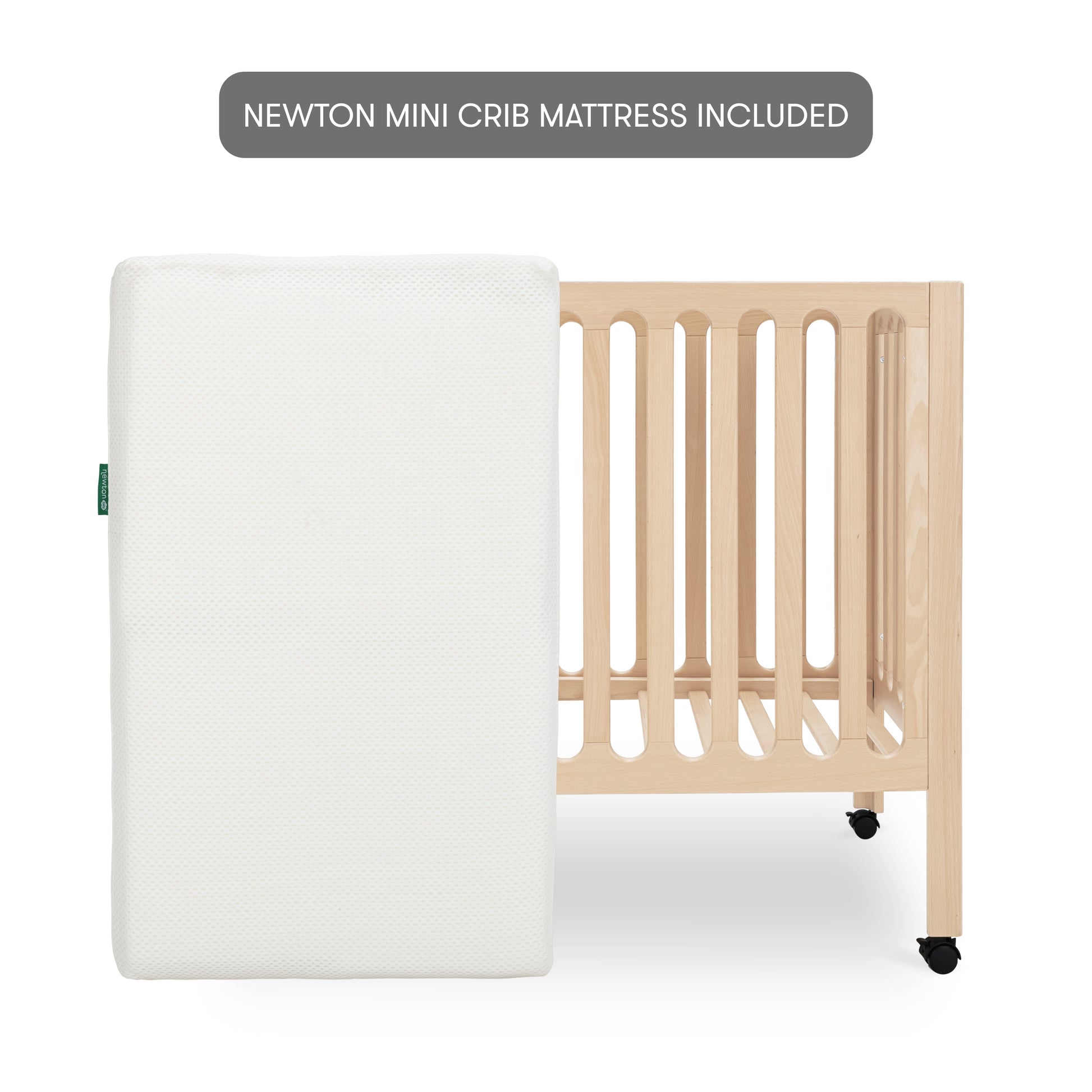 The Newton Galileo Mini Crib with Newton Mattress by Newton Baby, shown in light beech wood with wheels behind a white mattress, highlights the included NEWTON MINI CRIB MATTRESS and stylish, convenient portable design.