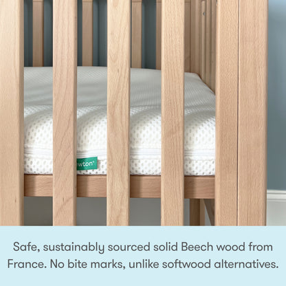 A close-up of the Newton Galileo Mini Crib with Newton Mattress by Newton Baby shows solid French Beech wood slats and a white mattress, emphasizing its portable, safe design and superior durability over softwood cribs.