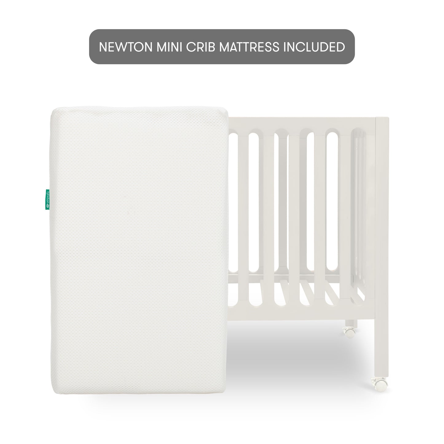 The Newton Galileo Mini Crib with Newton Mattress by Newton Baby is shown in white with vertical slats, and a white rectangular mattress leaning against it. A label above says, “NEWTON MINI CRIB MATTRESS INCLUDED.”.