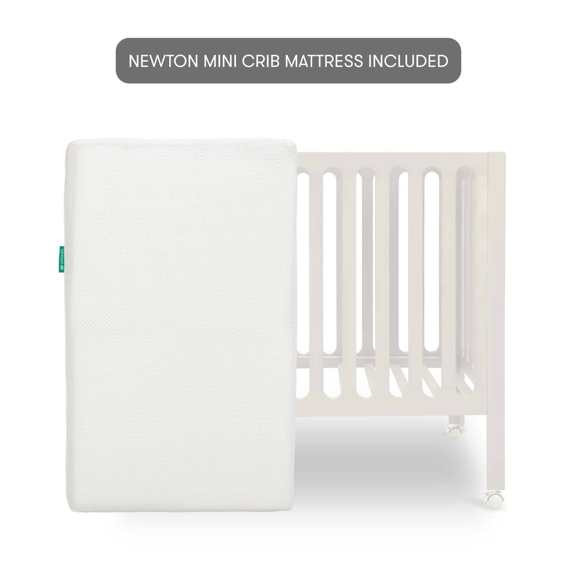The Newton Galileo Mini Crib with Newton Mattress by Newton Baby is shown in white with vertical slats, and a white rectangular mattress leaning against it. A label above says, “NEWTON MINI CRIB MATTRESS INCLUDED.”.