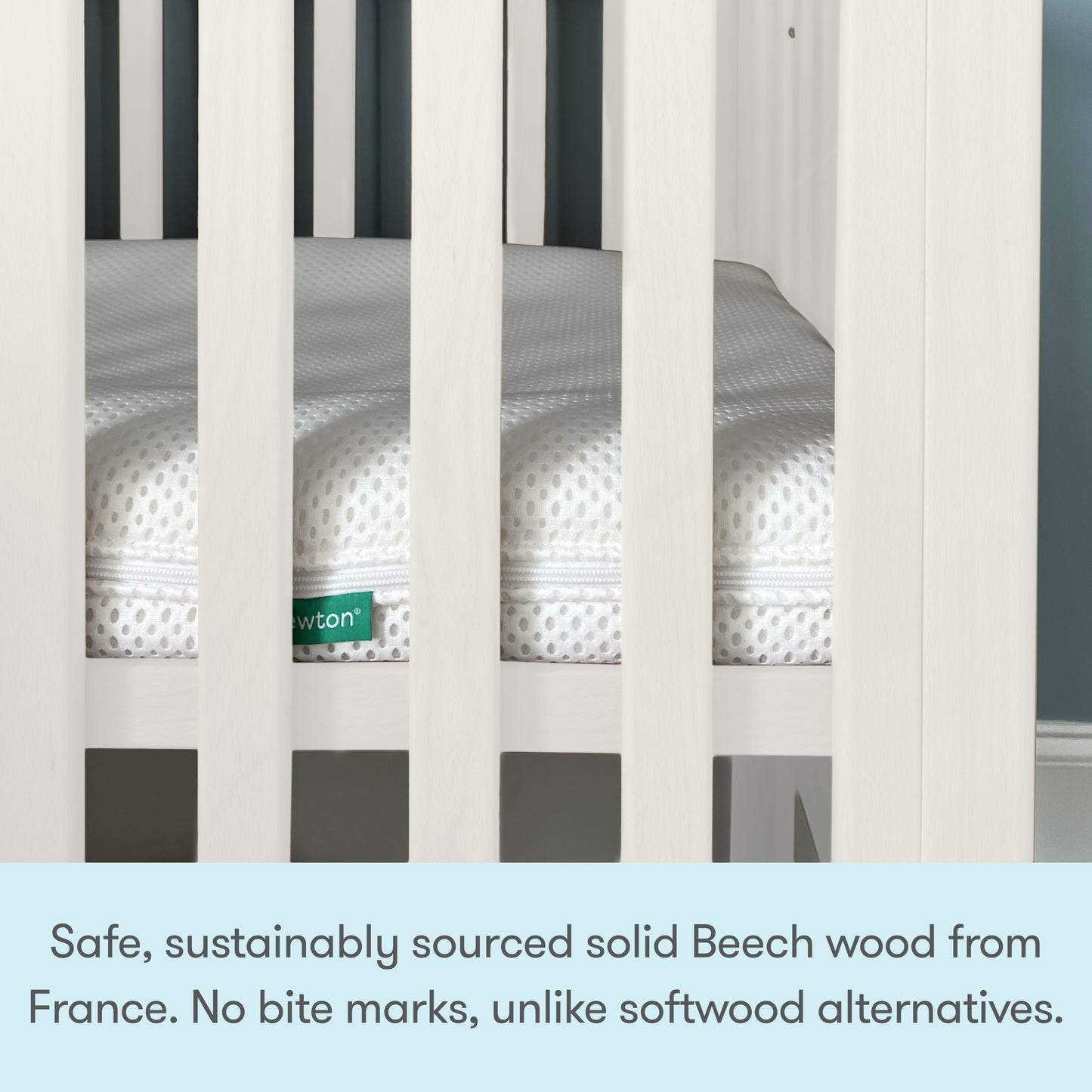 Close-up of a white Newton Galileo Mini Crib with Newton Mattress. Text below reads: Crafted from safe, sustainably sourced solid Beech wood from France—no bite marks like softwood alternatives. From Newton Baby.