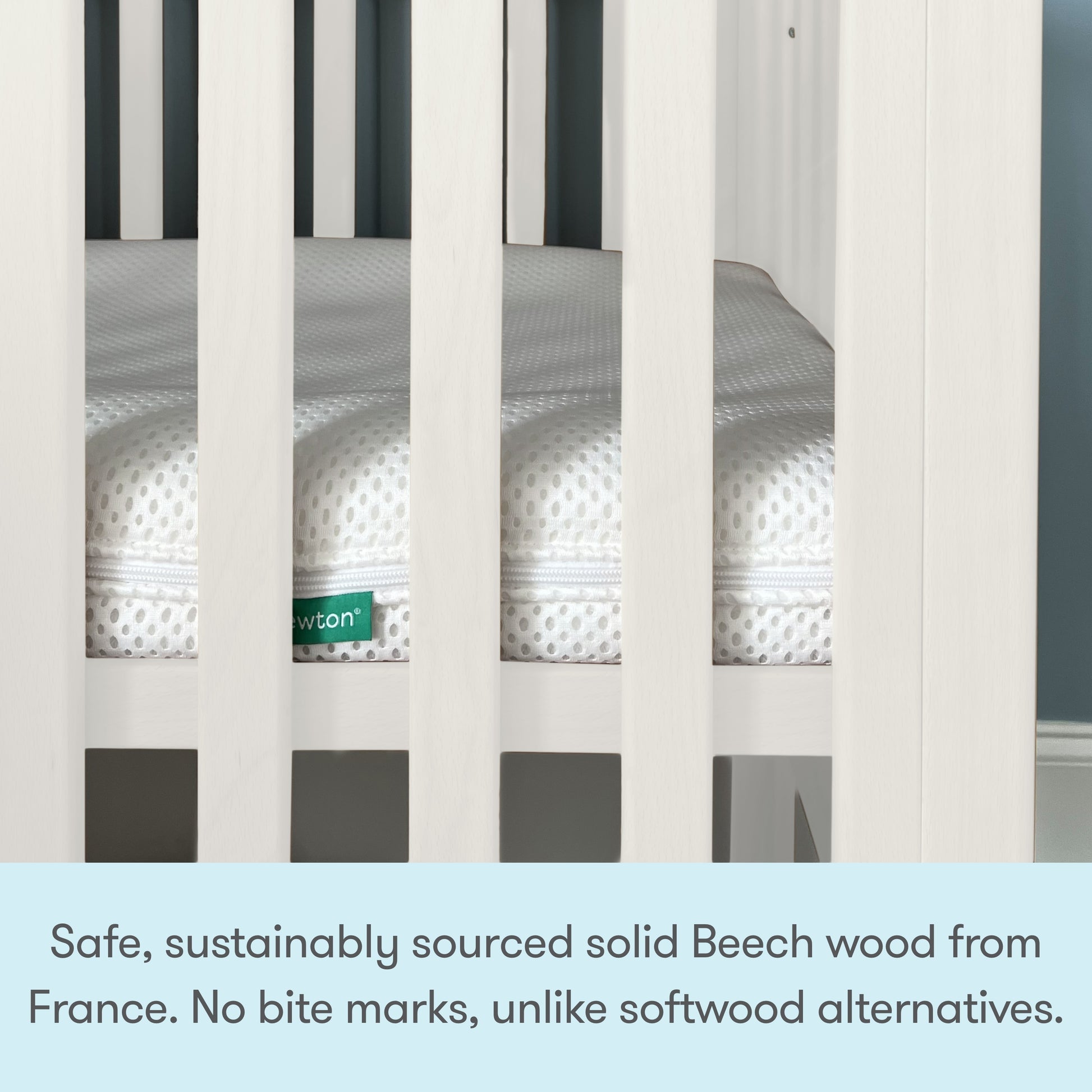 Close-up of a white Newton Galileo Mini Crib with Newton Mattress. Text below reads: Crafted from safe, sustainably sourced solid Beech wood from France—no bite marks like softwood alternatives. From Newton Baby.