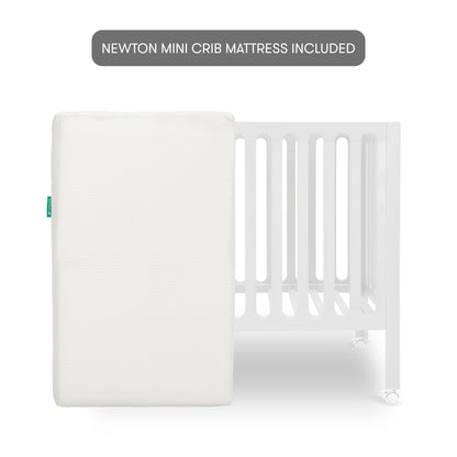 The Newton Galileo Mini Crib with Newton Mattress by Newton Baby features a white crib with vertical slats and wheels, shown behind a white mini crib mattress. A grey label above states: NEWTON MINI CRIB MATTRESS INCLUDED.