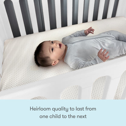 A baby in a light gray sleepsuit rests on a Newton Galileo Mini Crib with Newton Mattress by Newton Baby. Text below reads: Heirloom quality to last from one child to the next.