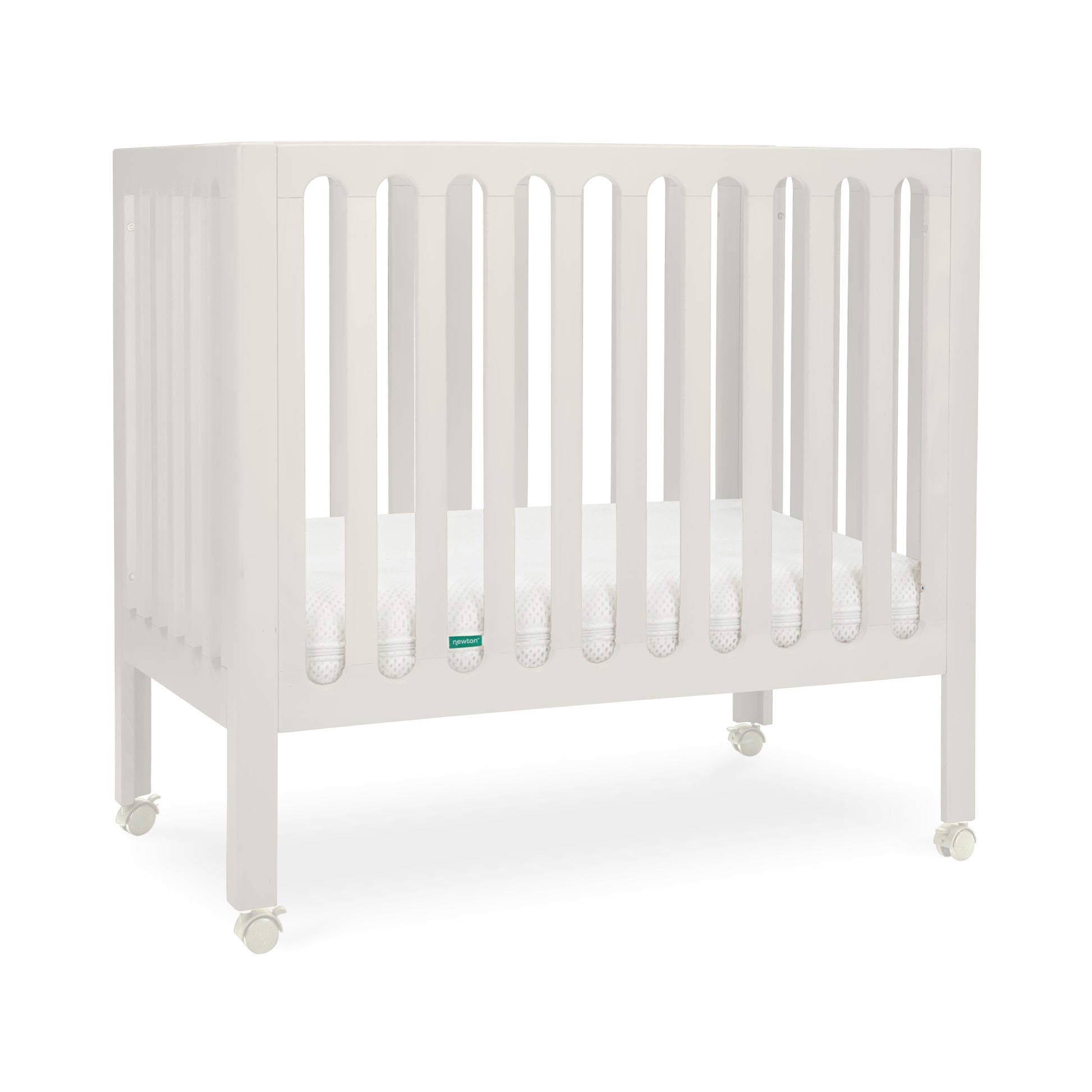 newton warm white crib with mattress inside and wheels on white background.