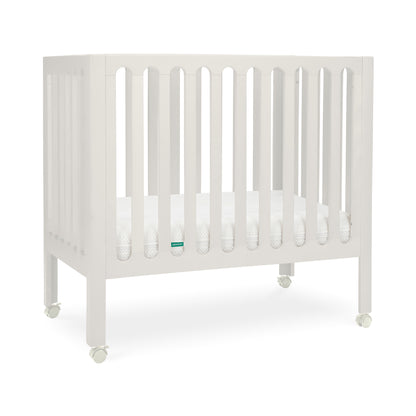 newton warm white crib with mattress inside and wheels on white background.
