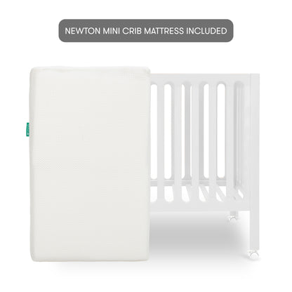 White modern crib on wheels with mattress leaned against crib, isolated on a plain background. With text "newton mini crib mattress included"