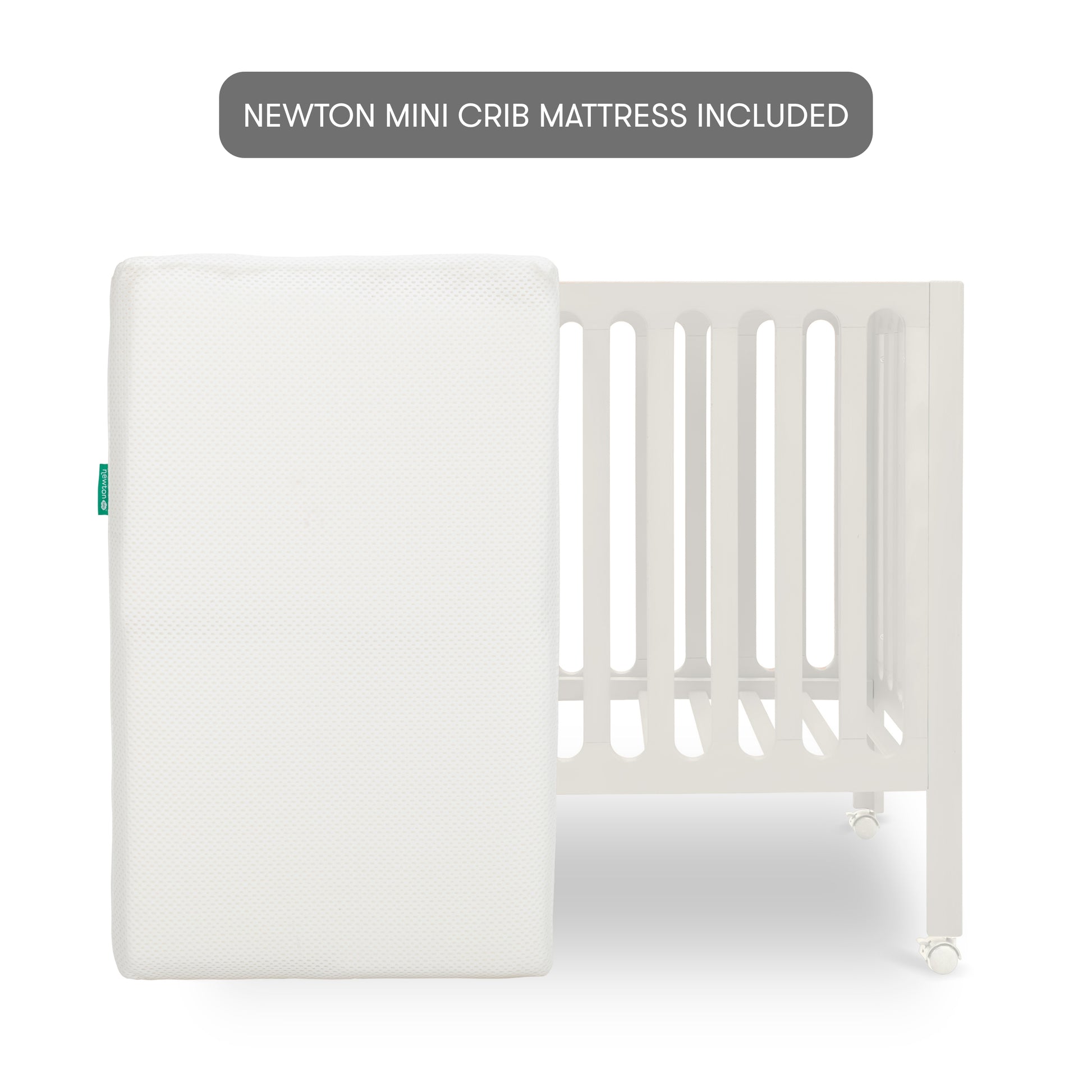 Warm White modern baby crib on wheels with a mattress stood up in front of it with text "newton mini crib mattress included".