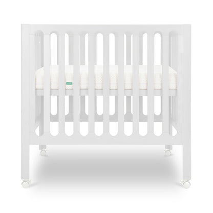 White modern crib on wheels with visible mattress, isolated on a plain background.