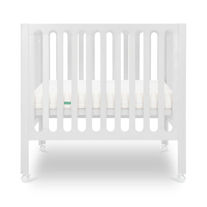 White modern crib on wheels with visible mattress, isolated on a plain background.