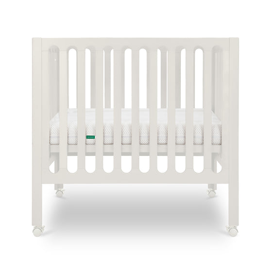 Warm White modern baby crib with a thin mattress on wheels.