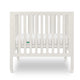 Warm White modern baby crib with a thin mattress on wheels.