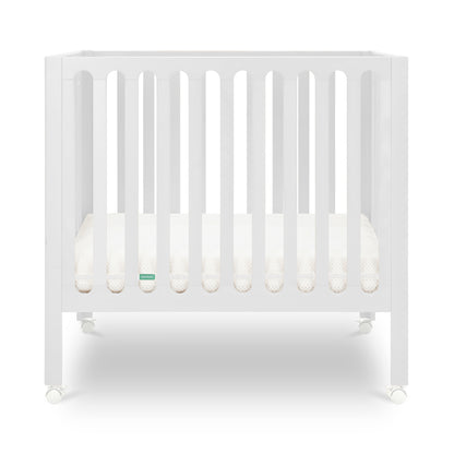 White modern crib on wheels with visible mattress, isolated on a plain background.