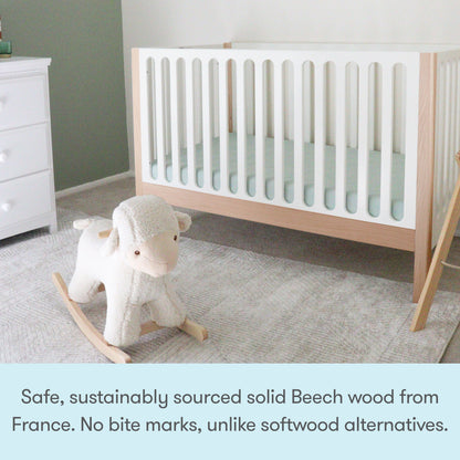 A modern nursery featuring the Newton Galileo Convertible Crib by Newton Baby in white and wood, grey carpet, white dresser, and plush rocking sheep. Made from durable, sustainably sourced solid Beech wood from France—no bite marks like softwood cribs.