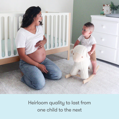 A pregnant woman smiles at a toddler on a plush rocking sheep in a bright nursery with the Newton Galileo Convertible Crib by Newton Baby. Text reads: Heirloom quality to last from one child to the next.