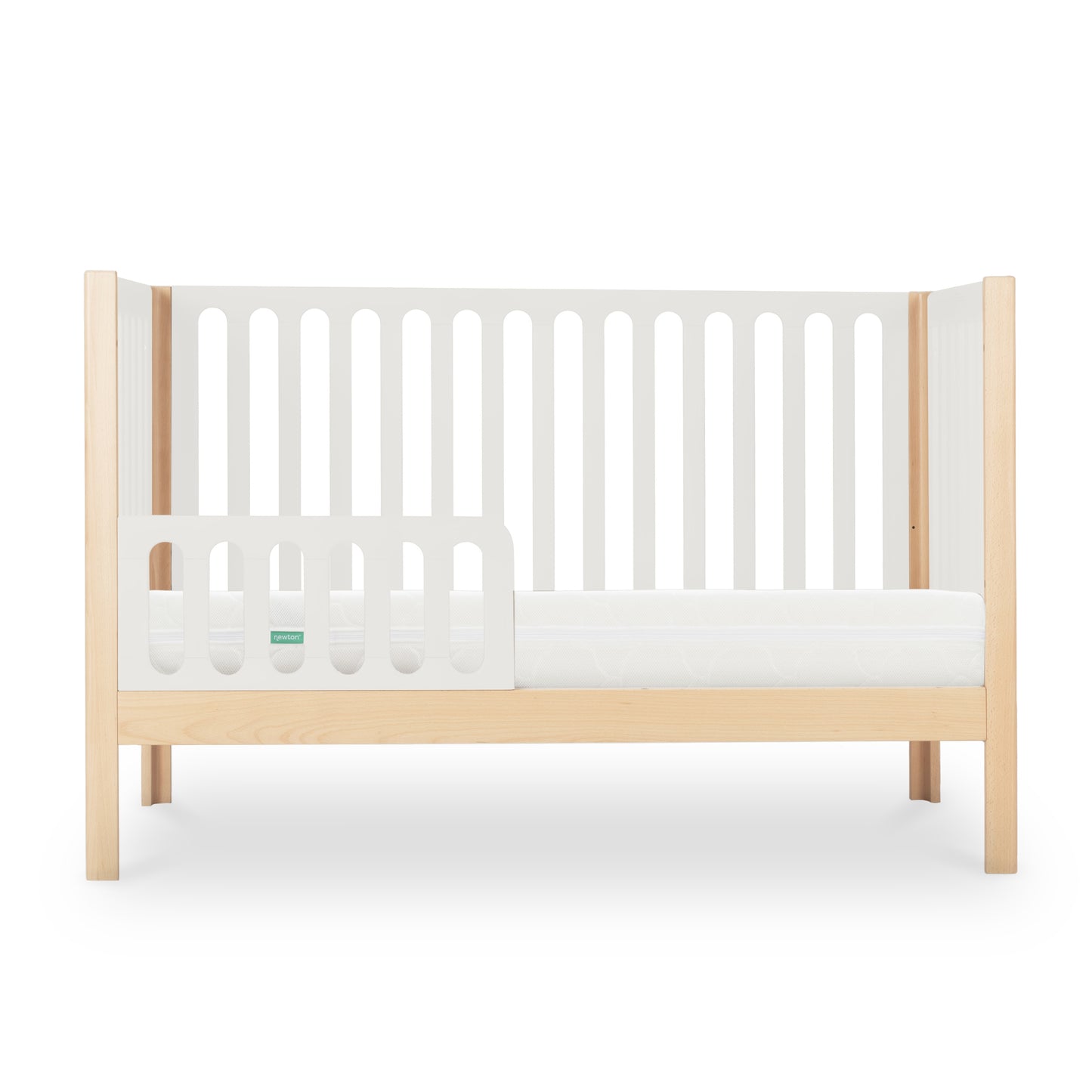 The Newton Galileo Convertible Crib by Newton Baby features light beech wood legs, white slatted sides, and a partial side rail. This stylish 3-in-1 crib easily converts to a toddler bed. Shown with a white mattress against a plain background.