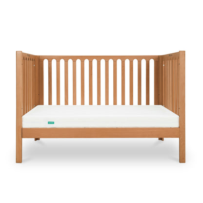 The Newton Galileo Convertible Crib by Newton Baby, made of beech wood with vertical slats and a white mattress, is shown against a plain white background. It easily converts to a toddler bed for long-lasting versatility.