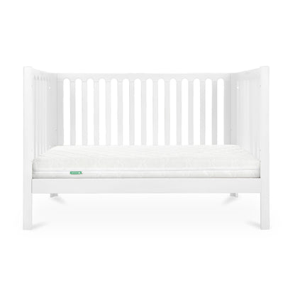 A simple white baby crib with a clean mattress displaying a small green 'Newton' logo on its corner.