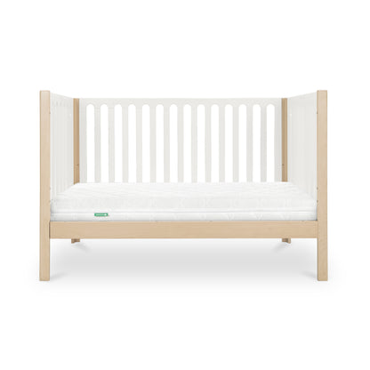 The Newton Baby Newton Galileo Convertible Crib features light beech wood legs and frame, white slatted sides, a white mattress, and offers toddler bed conversion for long-term use. Shown against a plain white background.