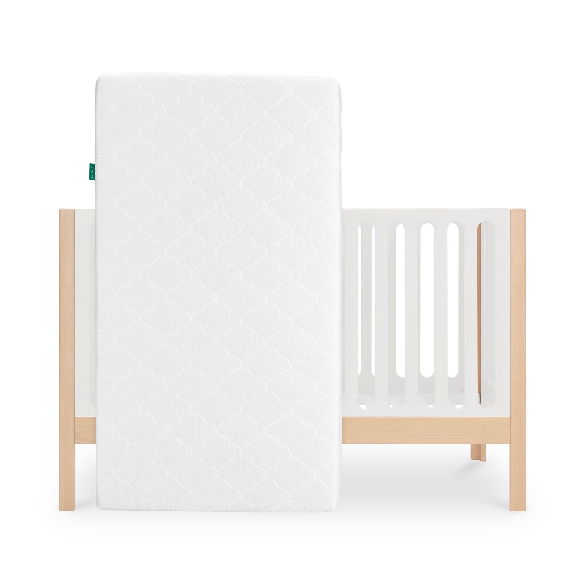 The Newton Galileo Convertible Crib by Newton Baby features modern beech wood with light slats and legs, paired with a white geometric-patterned crib mattress, and converts easily into a toddler bed as your child grows.