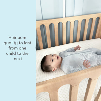 Baby in a gray sleeper lying on a crib mattress with text reading "Heirloom quality to last from one child to the next."