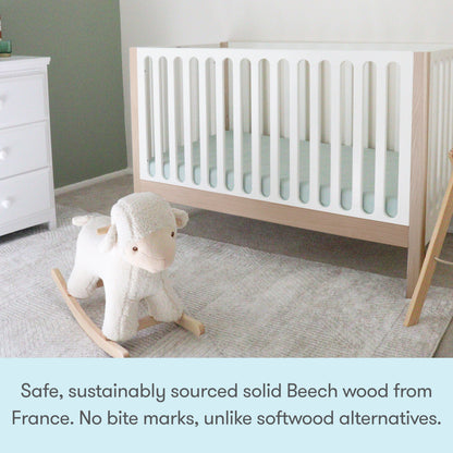 A modern nursery featuring the Newton Galileo Convertible Crib by Newton Baby (solid beech wood), a white dresser, and a plush rocking sheep on light gray carpet. Text highlights the crib’s safety, toddler bed conversion, and sustainable wood.