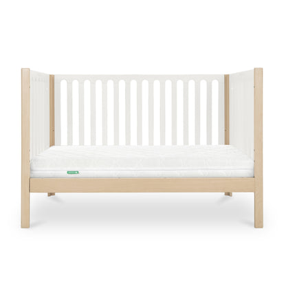The Newton Galileo Convertible Crib by Newton Baby features a modern beech wood frame with light wood legs, white slatted sides, and a white mattress. Shown from the front on a white background. Converts to a toddler bed for added versatility.